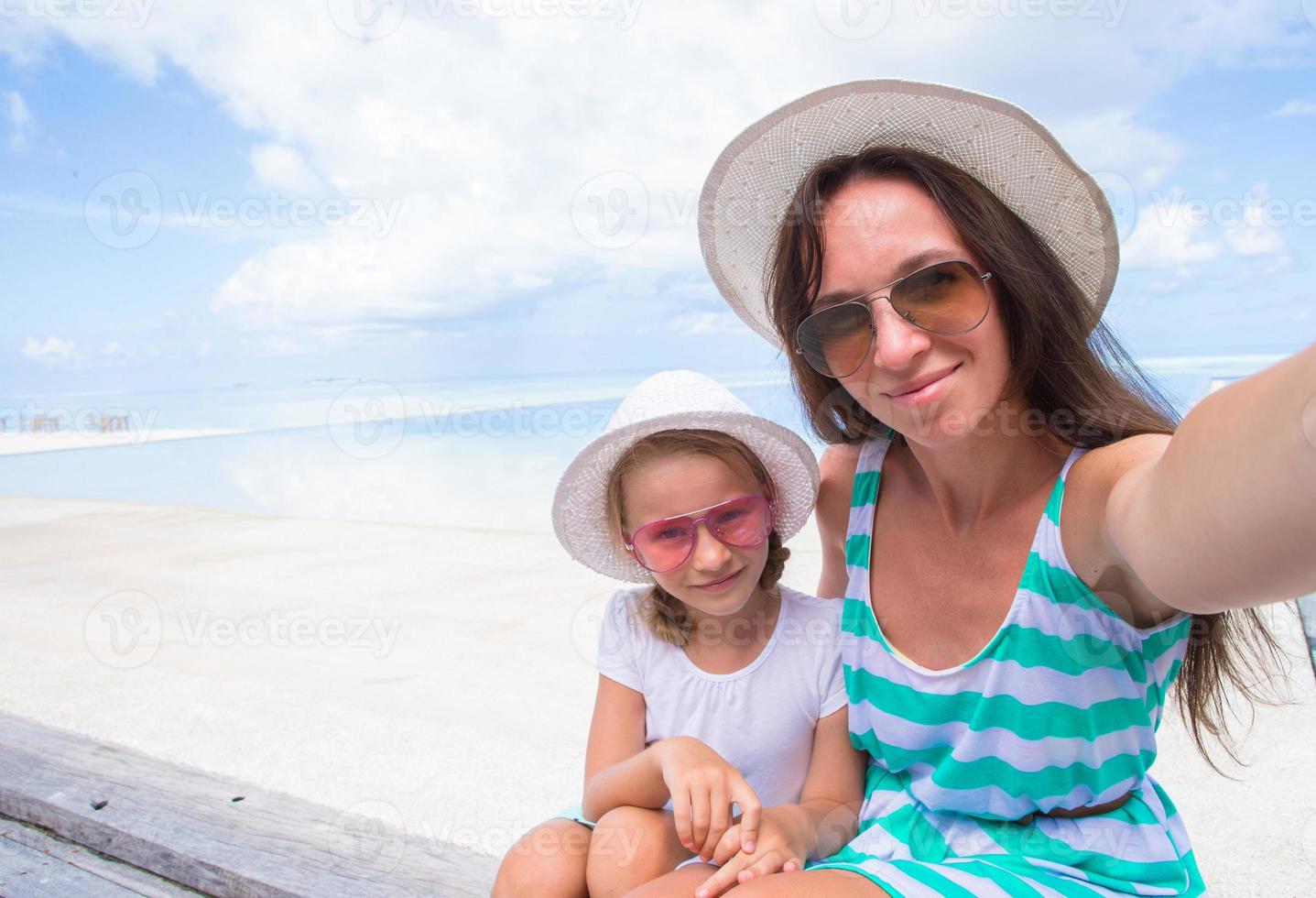 madre y niña tomando selfie en playa tropical foto