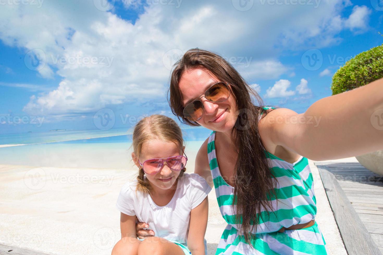 madre y niña tomando selfie en playa tropical foto