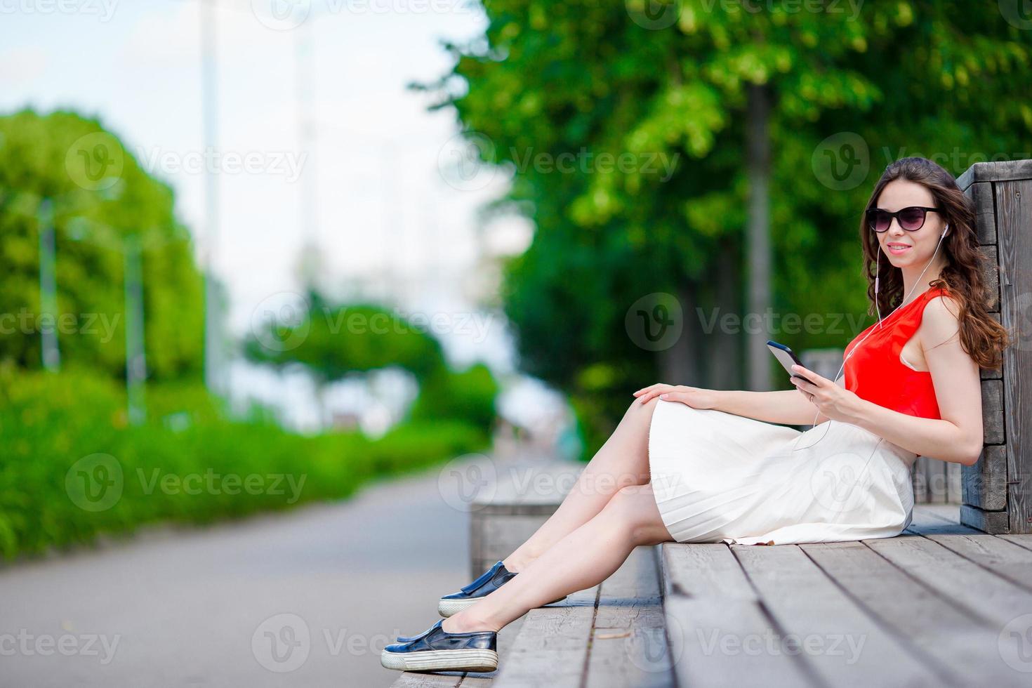 hermosa chica escuchando música por teléfono inteligente en vacaciones de verano. joven turista atractivo con teléfono móvil al aire libre disfrutando de las vacaciones. foto