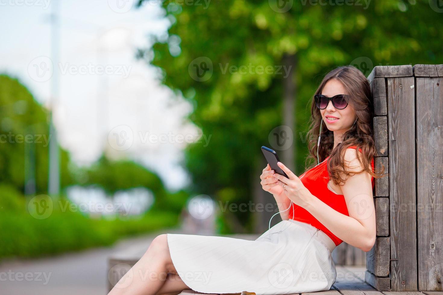 hermosa chica escuchando música por teléfono inteligente en vacaciones de verano. joven turista atractivo con teléfono móvil al aire libre disfrutando de las vacaciones. foto