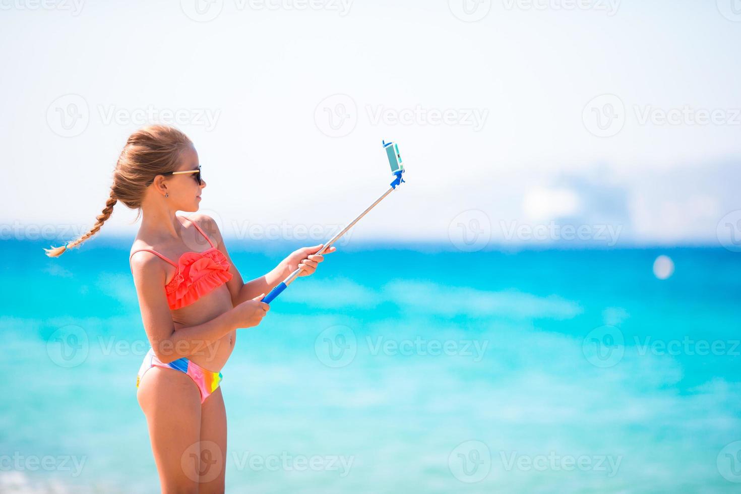 Little girl taking selfportrait by her smartphone on the beach. photo