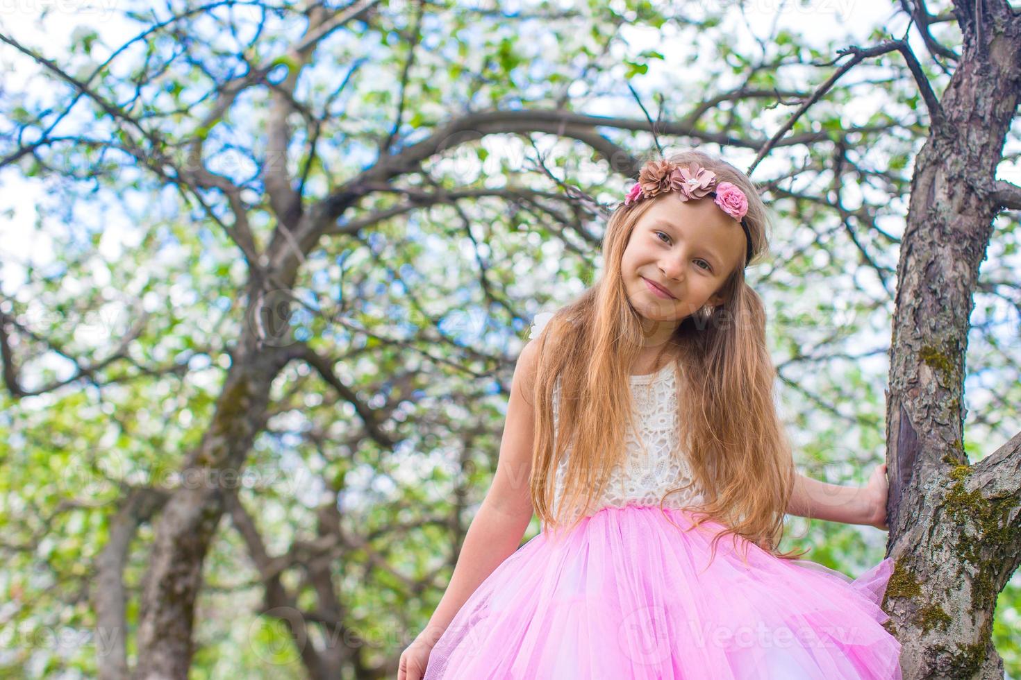 niña adorable sentada en un árbol floreciente en el jardín de manzanas foto