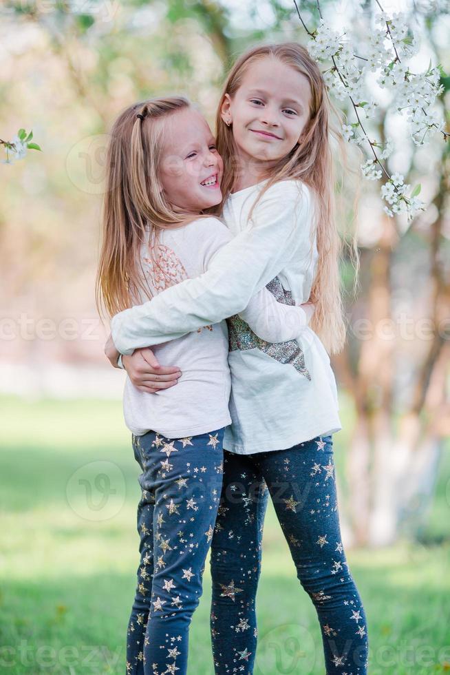Adorable little girls in blooming cherry tree garden on spring day photo