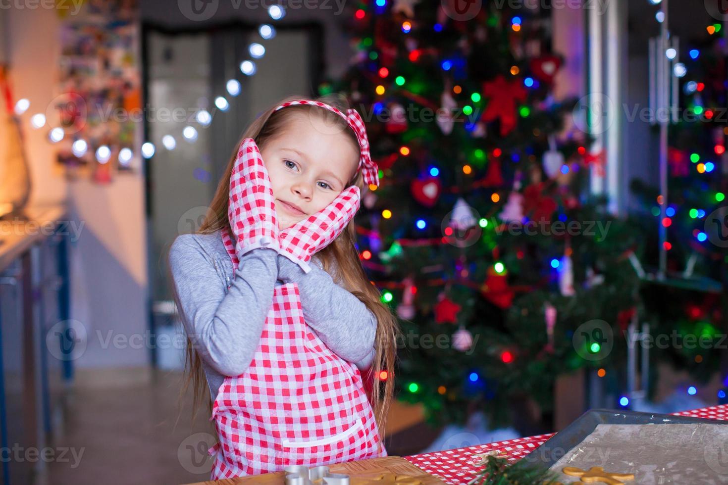 Adorable little girl in mittens baking Christmas gingerbread cookies photo