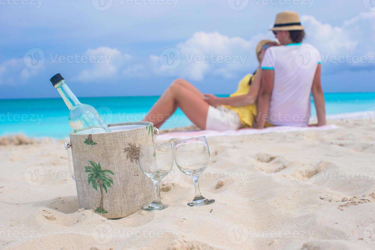 Bottle of white wine and two glasses background happy couple on sandy beach photo