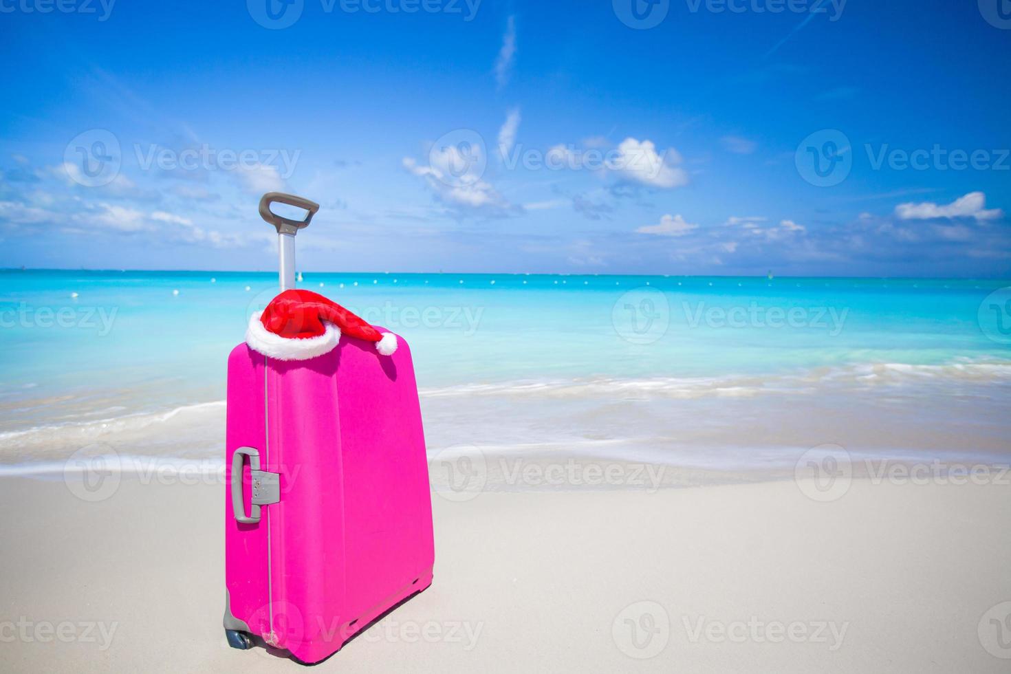 Closeup of pink suitcase and Santa Claus hat on beach photo