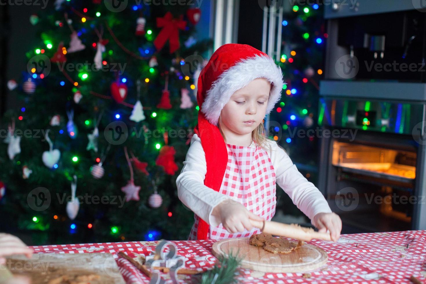 Little girl in Santa hat with rolling pin baking gingerbread cookies photo