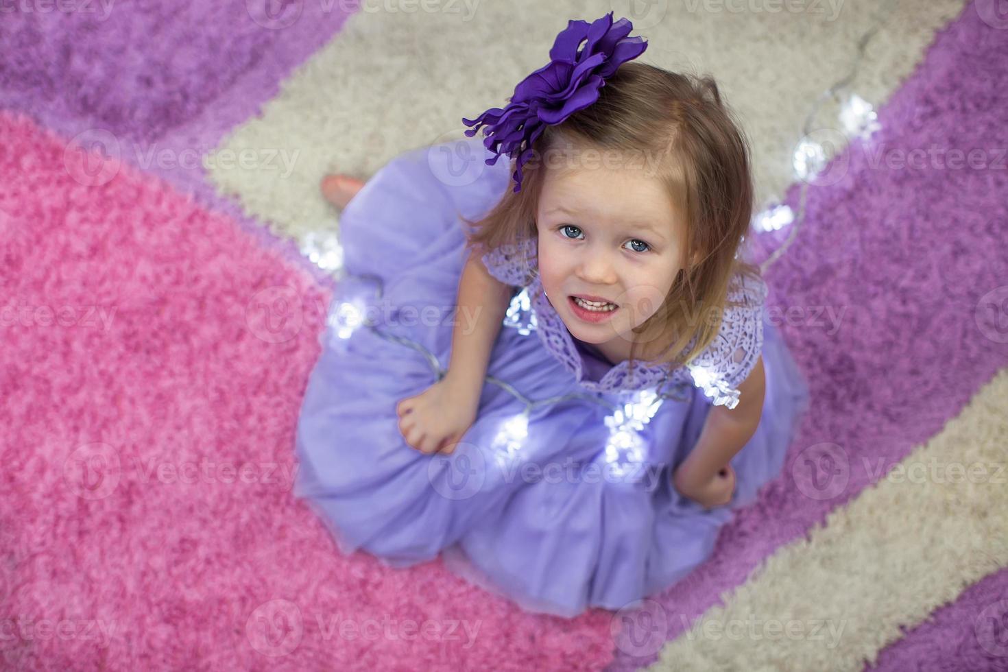 Little adorable girl in a lilac dress among garlands at home photo