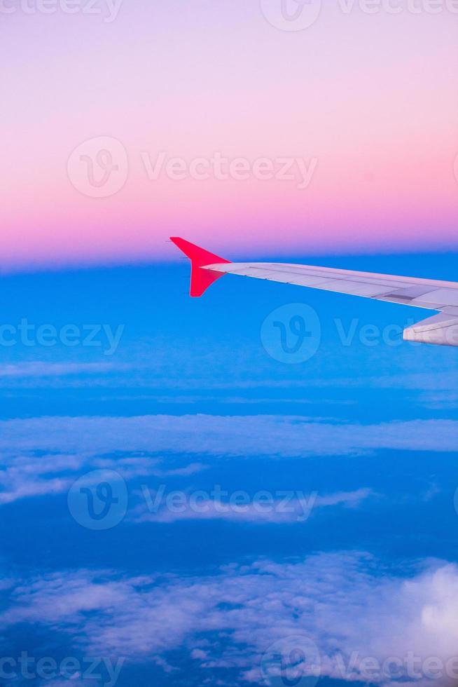 Wing of an airplane flying above the clouds in colorful sky photo