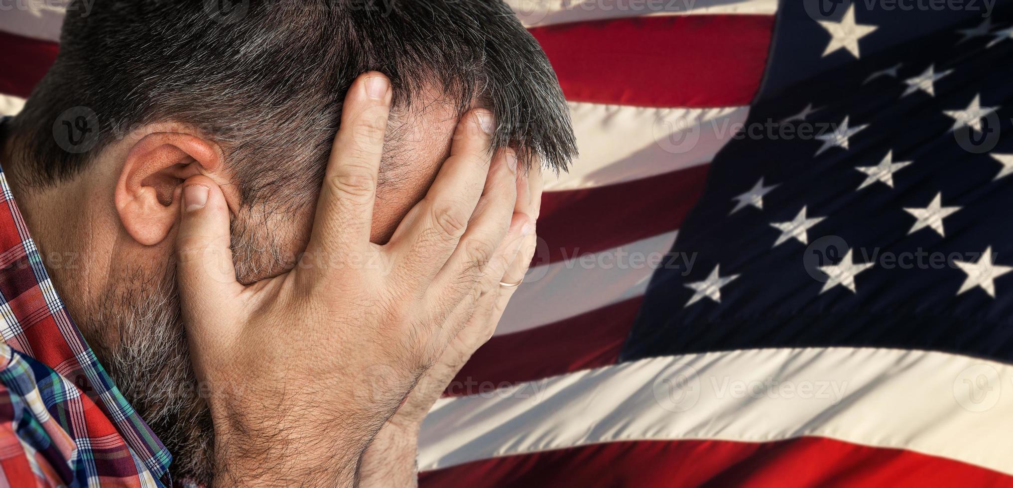 Veteran. Man in despair with face covered by hands in front of American flag photo