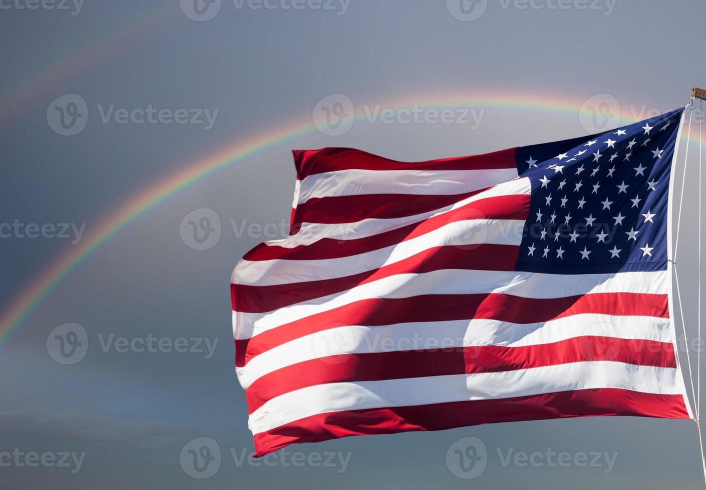 bandera americana contra un cielo nublado con un arco iris foto