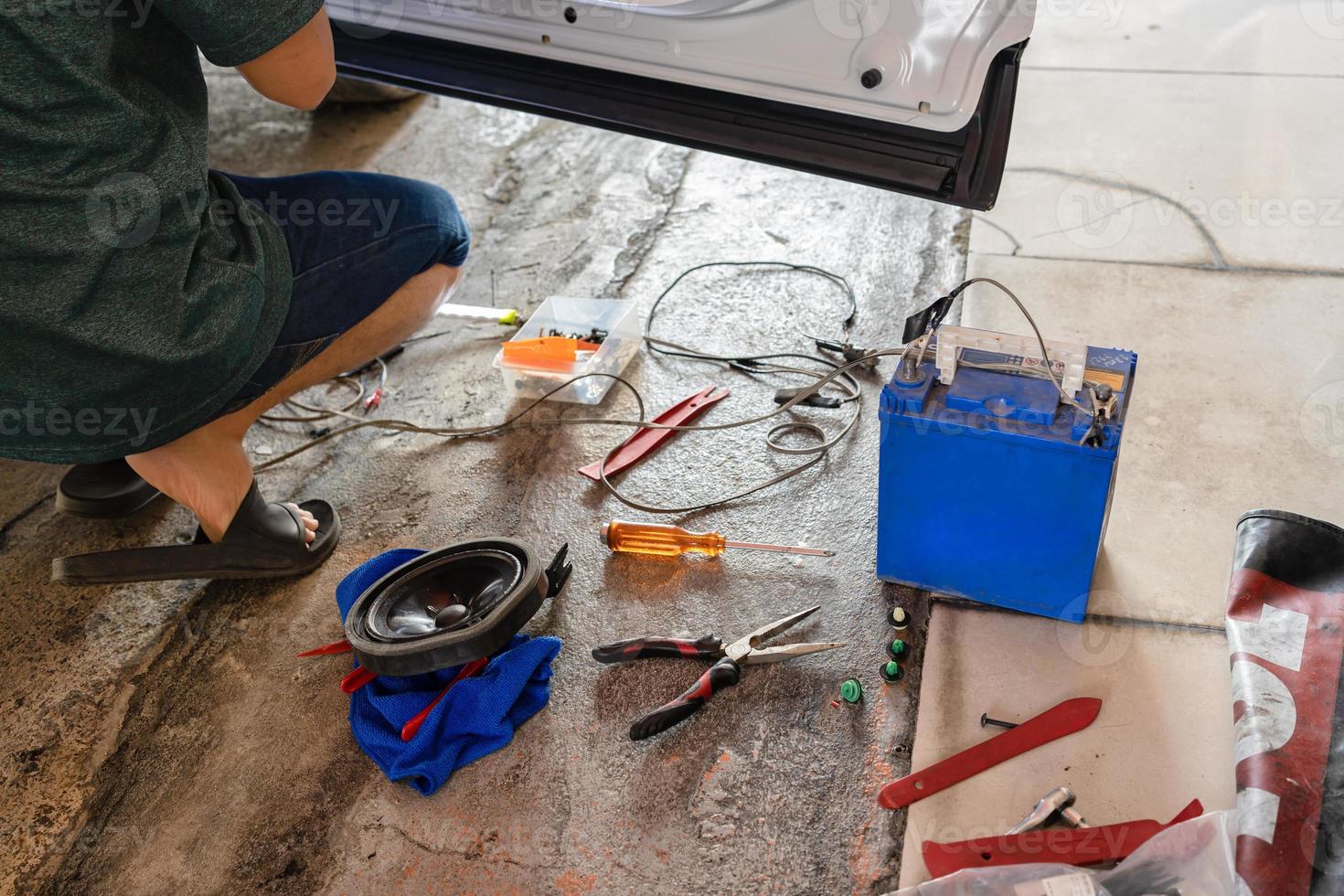 Mechanic man fixing the car with speaker equipment, pliers, wire and battery in workplace photo