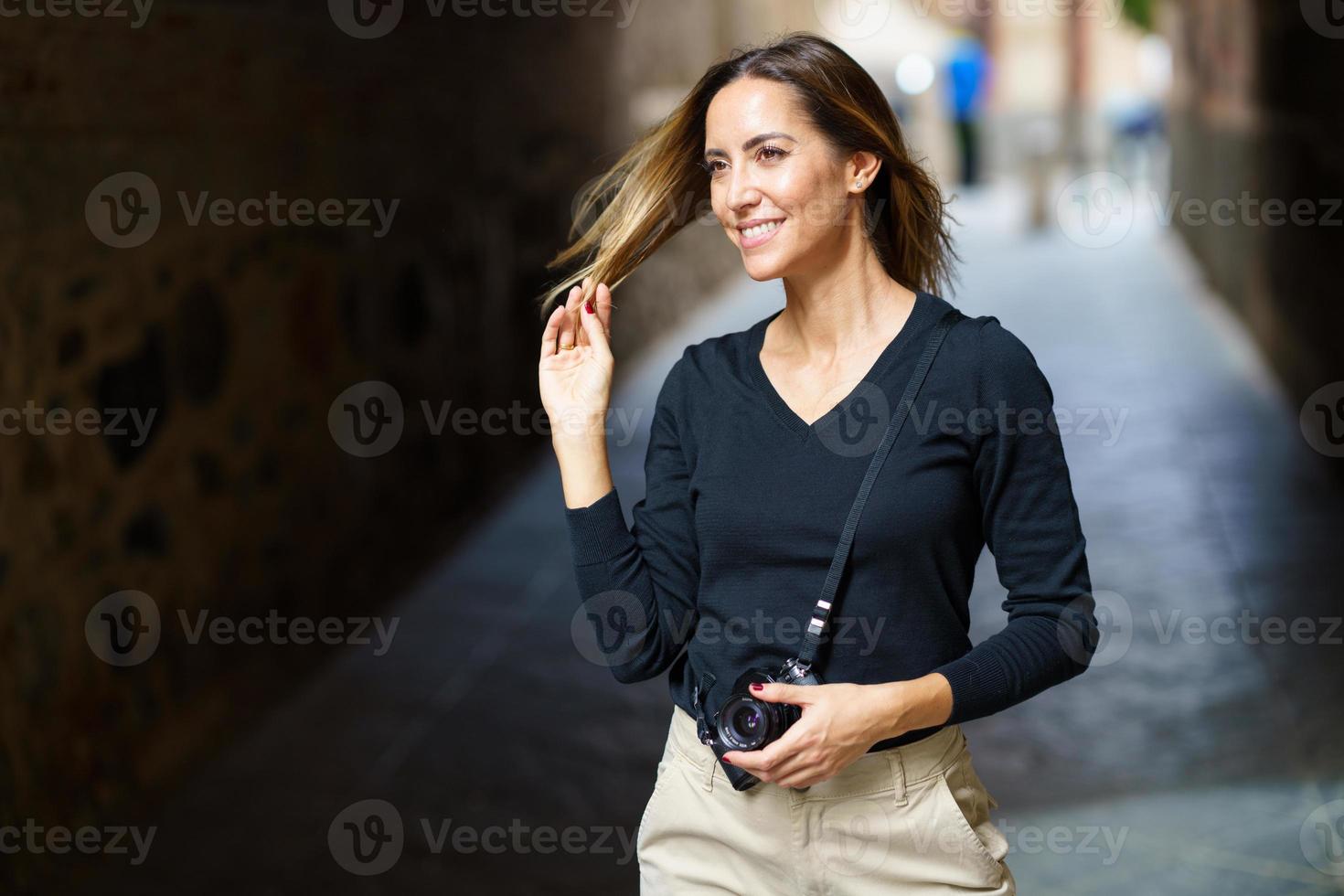 señora confiada con cámara sonriendo y tocando el cabello en la calle foto