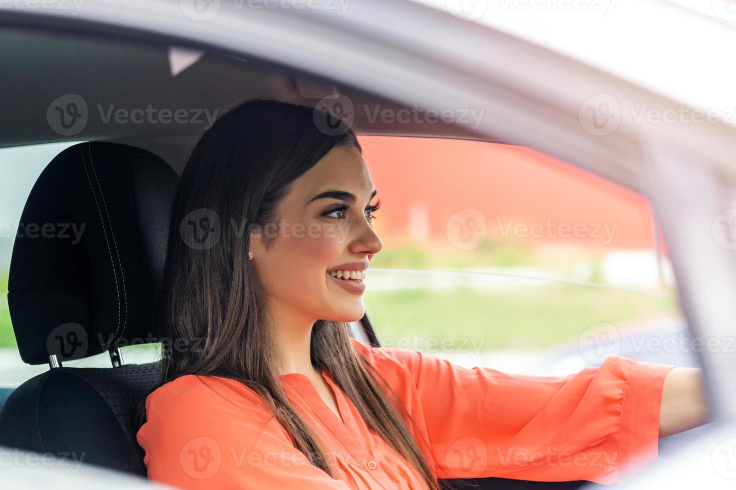 Cute young lady happy driving car. Image of beautiful young woman driving a car and smiling. Portrait of happy female driver steering car with safety belt photo