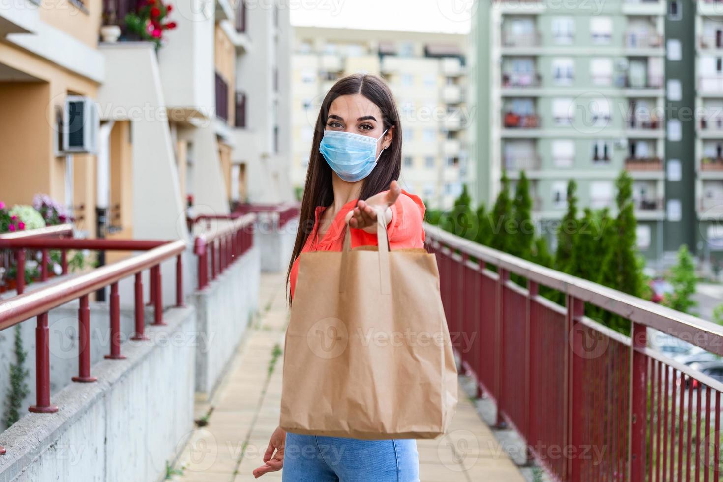 Young woman volunteer with a medical mask is holding a paper bag with food and vegetables. Donation, helping people in quarantine, coronavirus. Delivery shopping during Covid 19 outbreak. photo