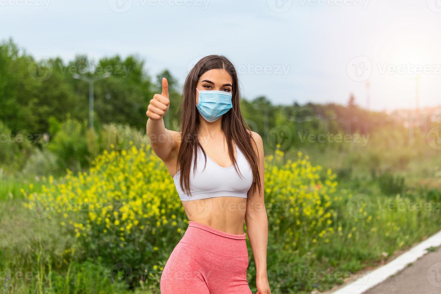 chica fitness, mujer joven con máscara médica estéril protectora en la cara mirando a la cámara y mostrando el pulgar hacia arriba. listo para hacer ejercicio durante covid 19, pandemia de coronavirus foto