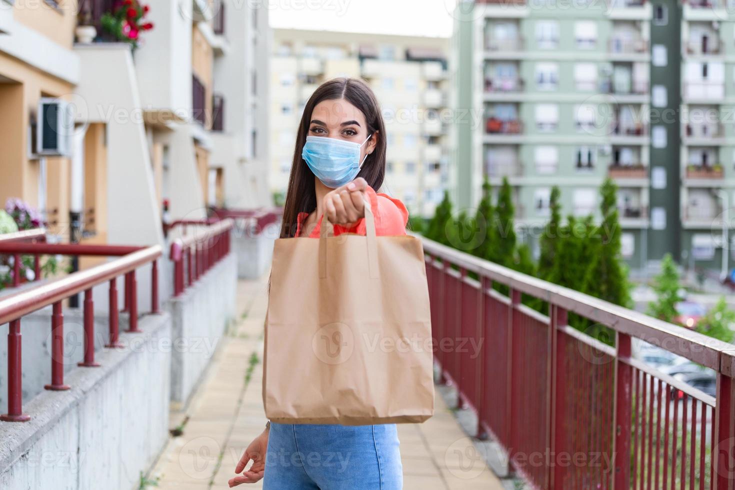 Young woman volunteer with a medical mask is holding a paper bag with food and vegetables. Donation, helping people in quarantine, coronavirus. Delivery shopping during Covid 19 outbreak. photo