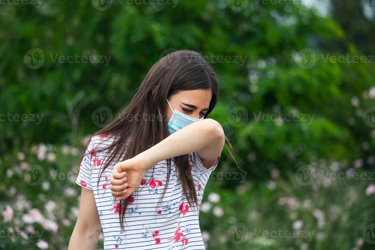 How to sneeze correctly. Woman with protective mask sneezes on the elbow. Concept of not spread of the virus. photo
