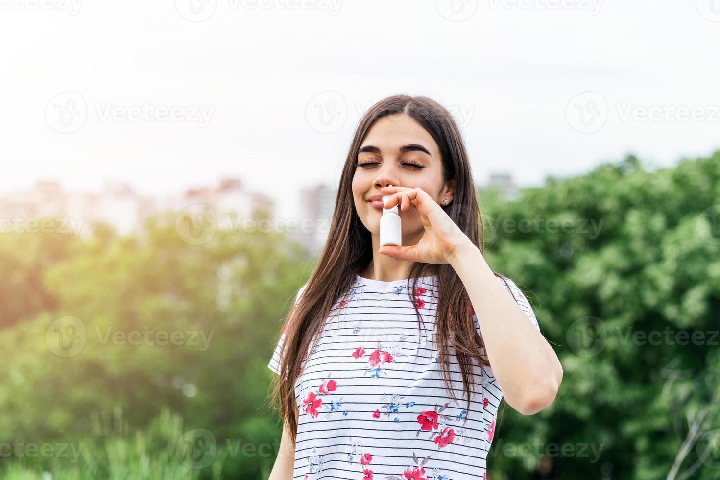 mujer joven que usa spray nasal para su polen y alergias a la hierba alivio de alergias árboles florecientes en el fondo. alergias estacionales de primavera y problemas de salud. foto