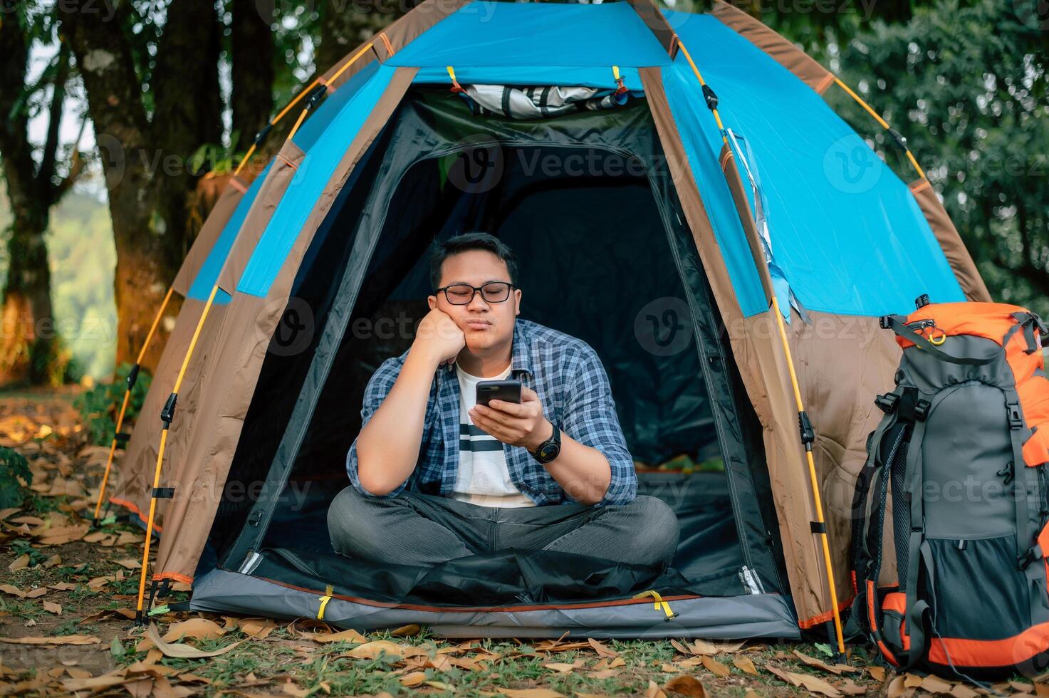 Portrait of Bored Asian traveler man glasses using smartphone in tent camping photo