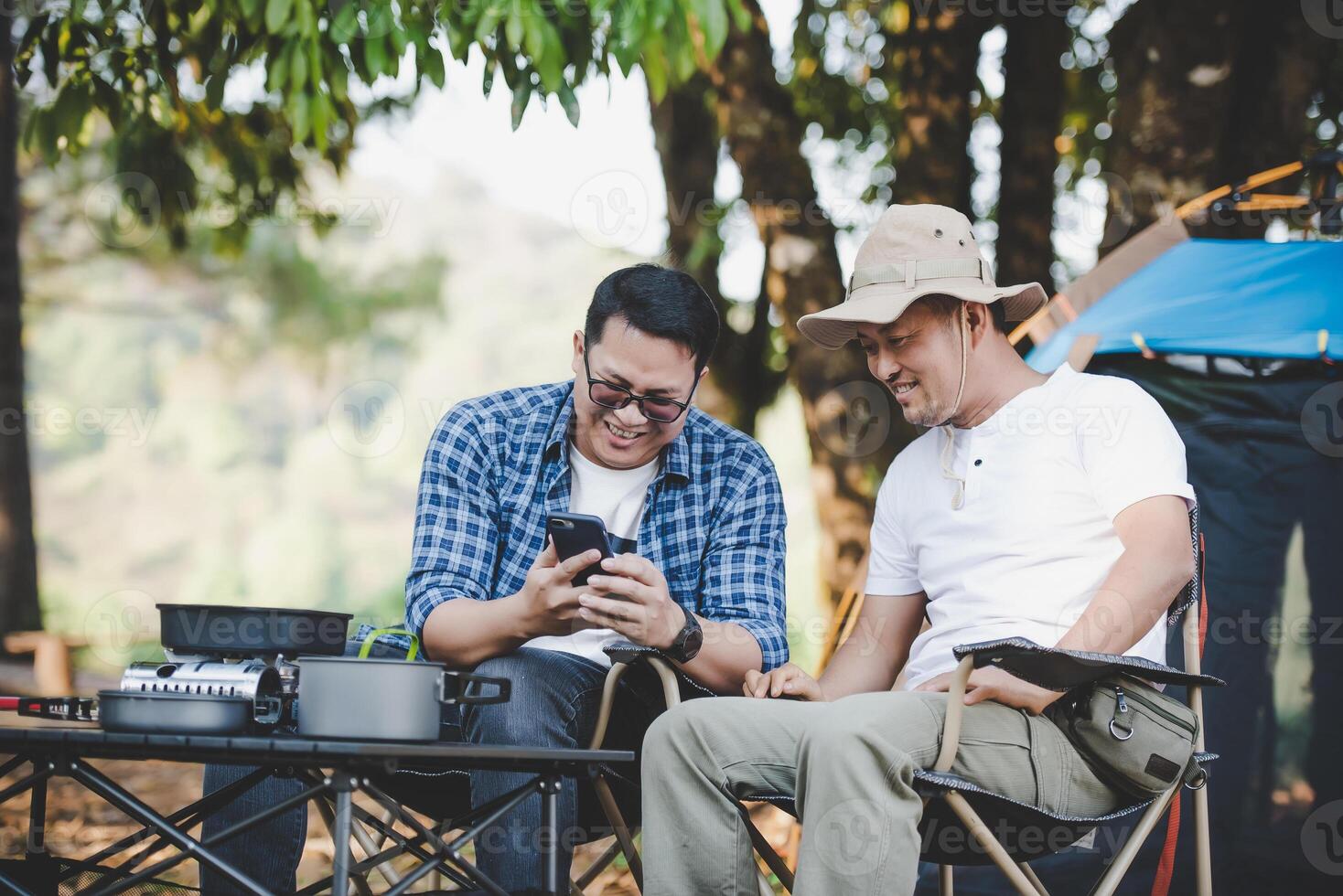 Man friends sitting on chair in the camp with talking and looking at smartphone photo