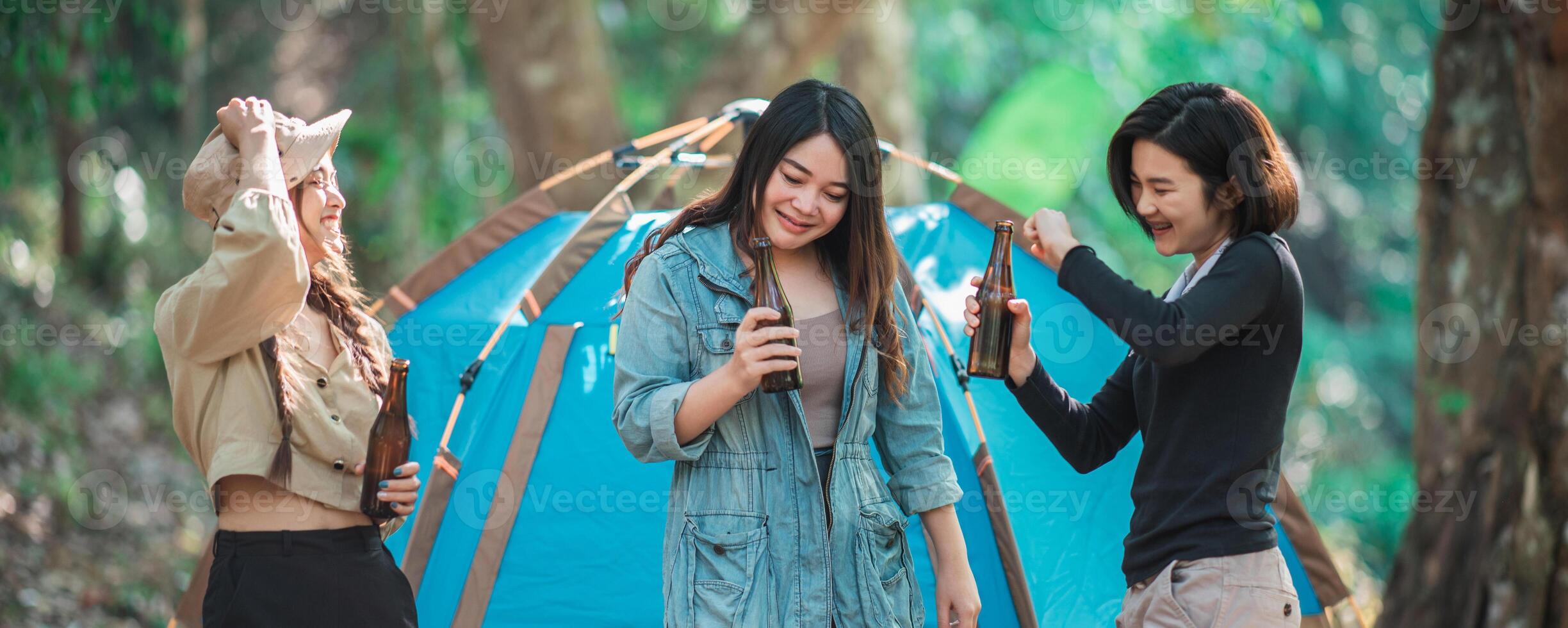 Young women cheer and drink beverage  front of camping tent photo