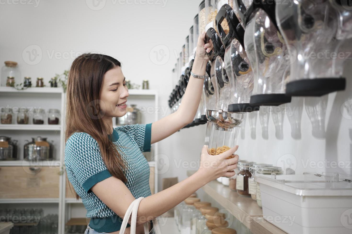A Caucasian female customer fills cereal foods in a glass jar, lever the reusable container on refill store shelves, zero-waste and plastic-free grocery, environment-friendly, sustainable lifestyles. photo