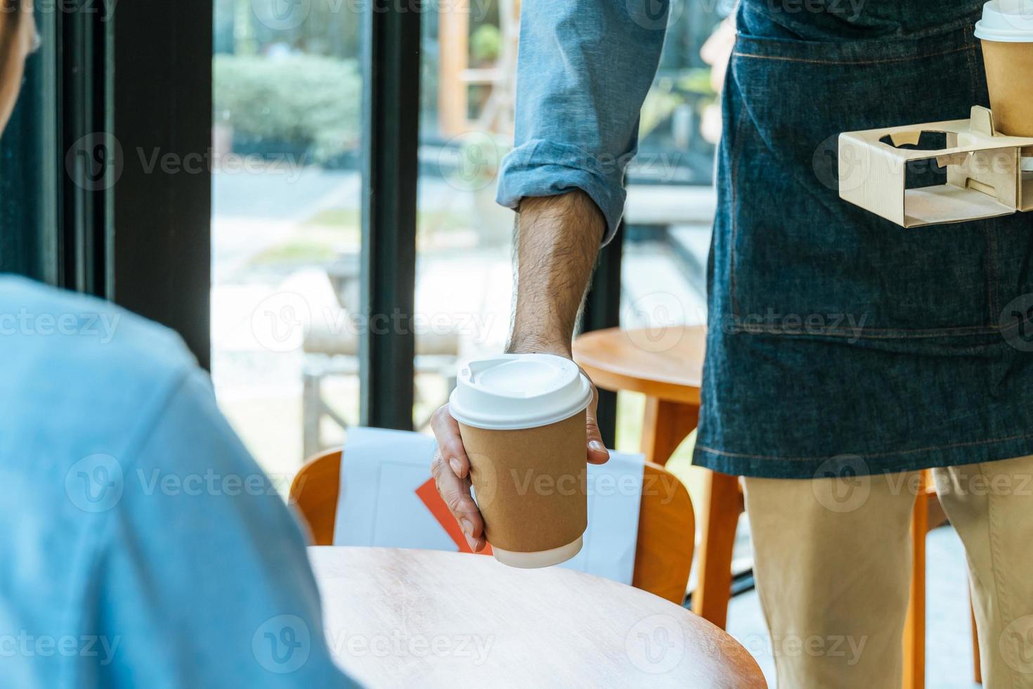 asian staff wearing apron serving hot black coffee cup to customer on table in cafe coffee shop, cafe restaurant, small business owner, service mind, new normal, food and drink delivery concept photo