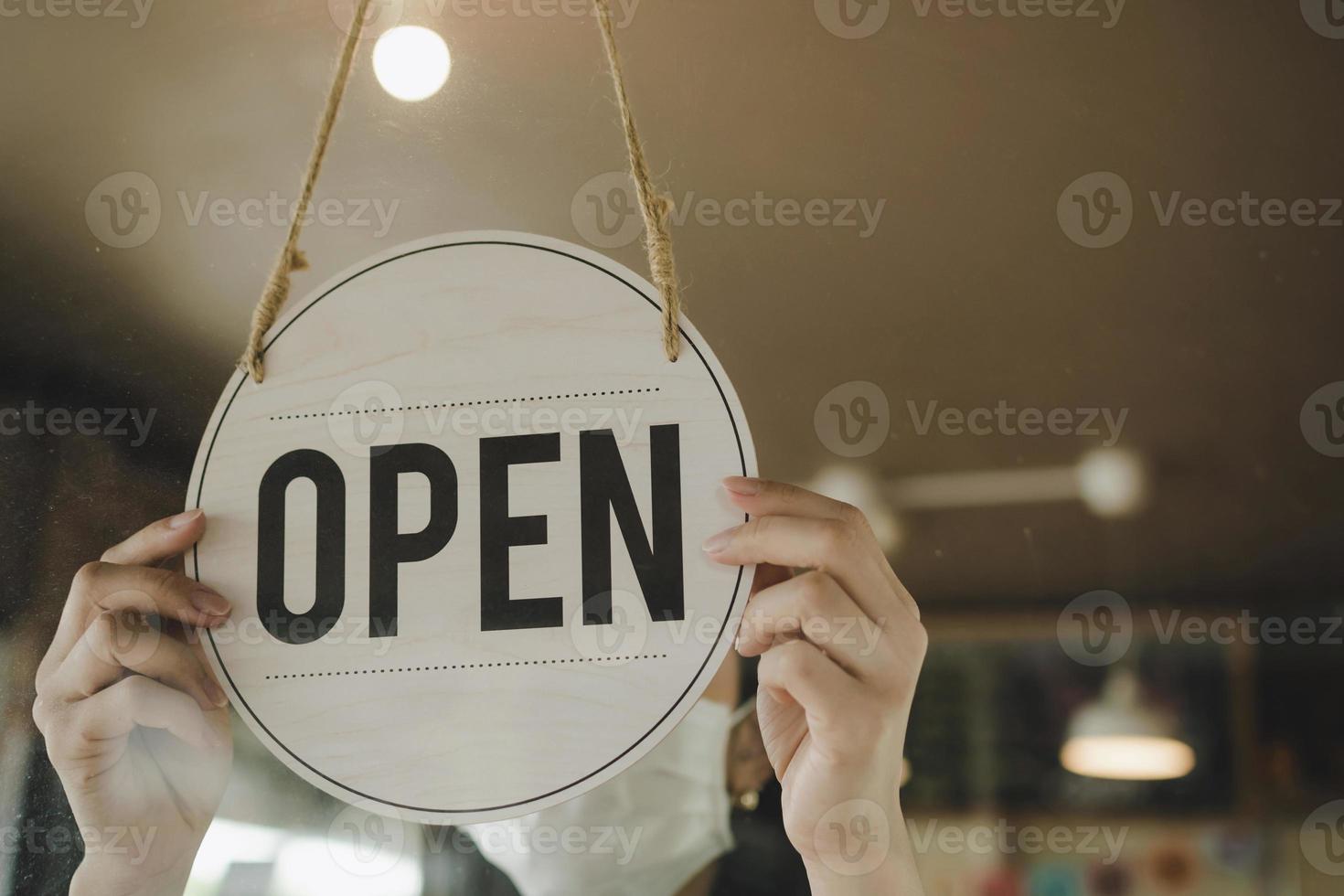 Open. barista, waitress woman wearing protection face mask turning open sign board on glass door in modern cafe coffee shop, cafe restaurant, retail store, small business owner, food and drink concept photo