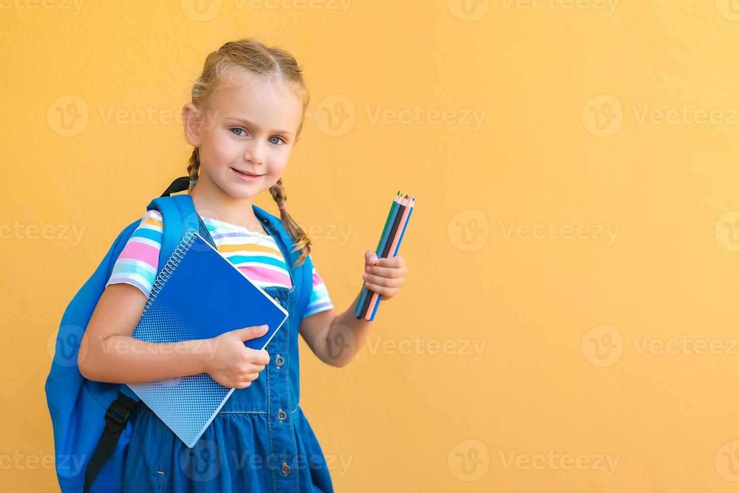 una colegiala sonriente con uniforme escolar sostiene lápices de colores, un cuaderno, un espacio de copia de pancarta de mochila aislado en un anuncio de fondo amarillo útiles escolares y papelería, regreso a la escuela foto