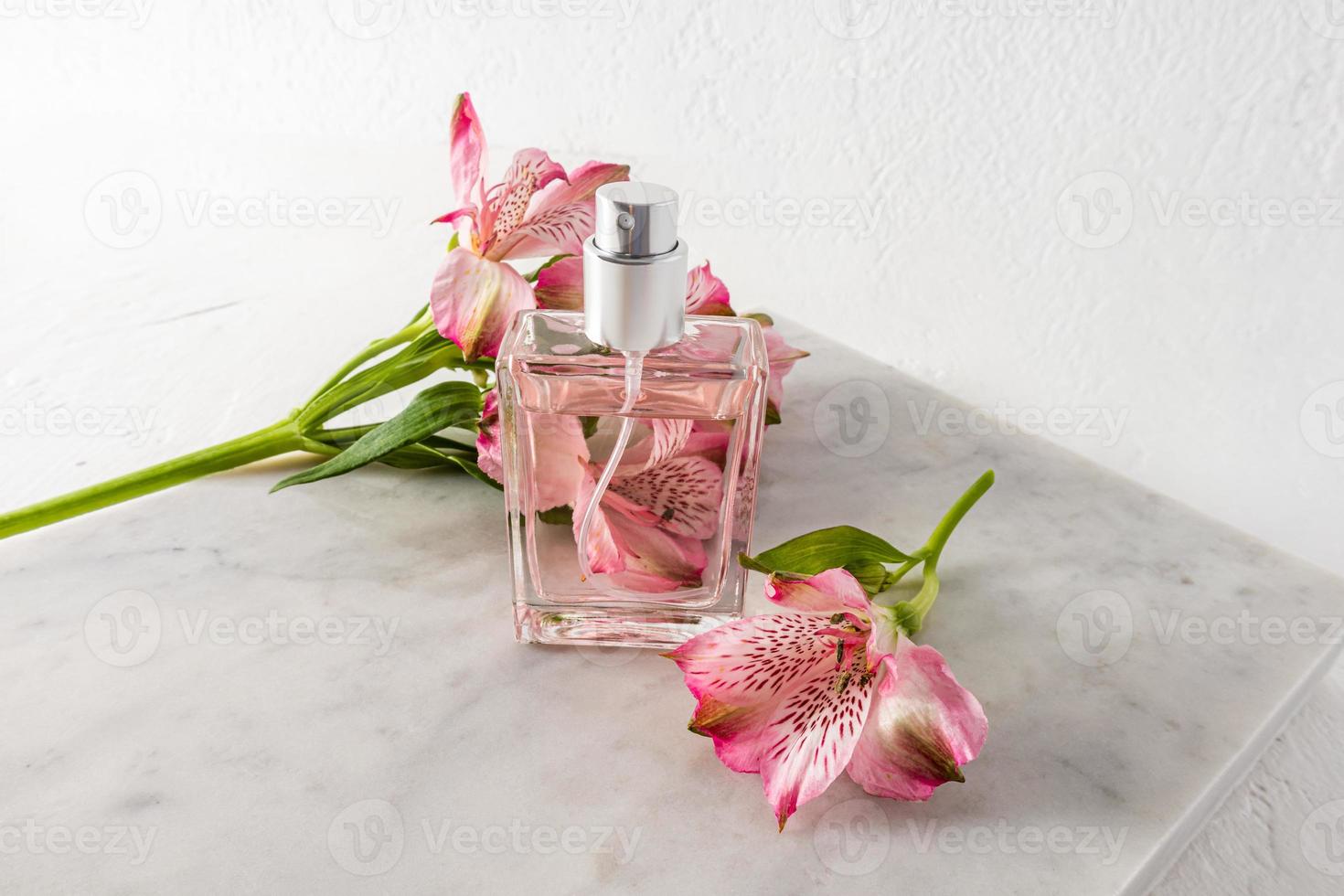 Beautiful bottle of women's perfume or spray against the background of pink flowers and marble white slab. presentation of the aroma. top view. photo