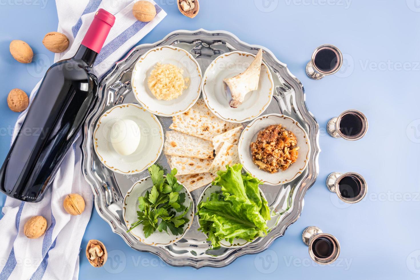 a silver platter with traditional Treats for the Jewish Passover, a bottle of red kosher wine and poured silver glasses. top view. blue background. photo