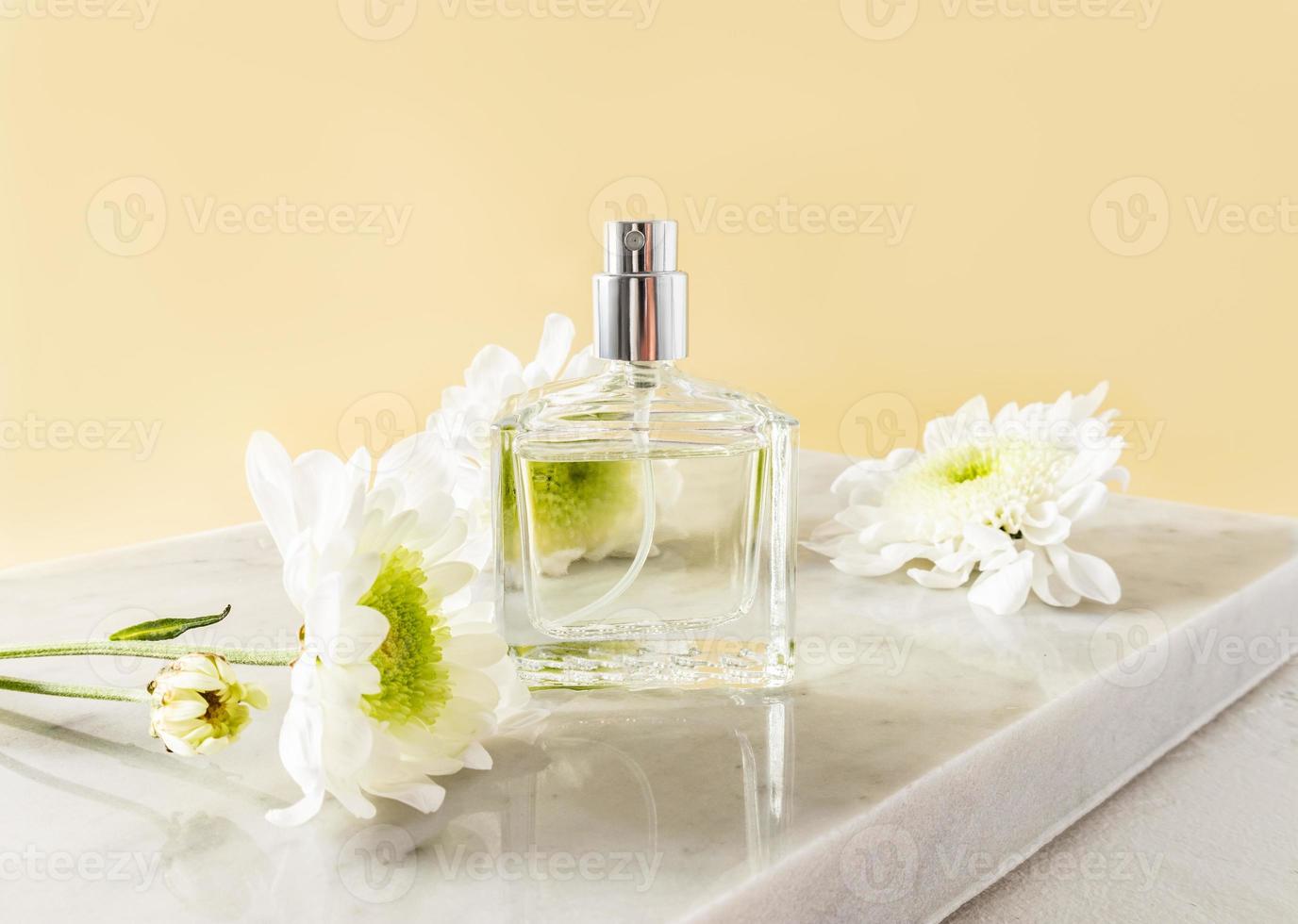 A beautiful bottle of women's perfume or spray stands on a white marble podium with white flowers. front view. An empty layout for your fragrance. photo