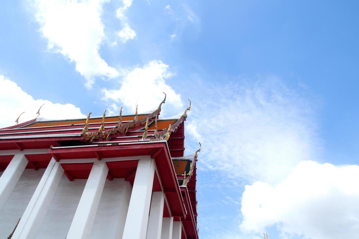 Beside white church with red triangle shape roof in Thai ancient style and bright blue sky with clouds, temple in Thailand. Row of poles beside the building. photo