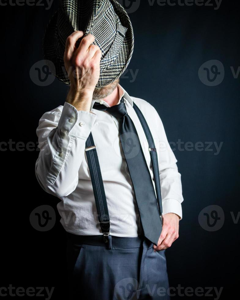 retrato de hombre de negocios con camisa de vestir blanca y tirantes poniéndose un viejo sombrero fedora. estilo vintage y moda retro del detective clásico. foto