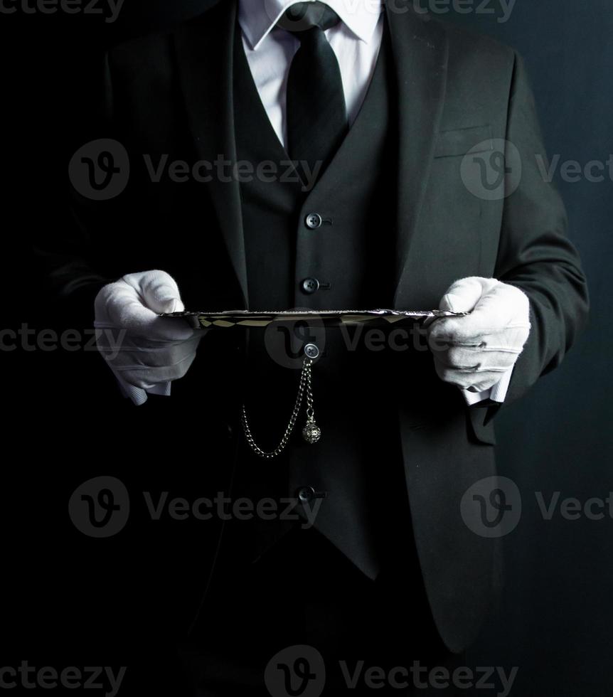 retrato de mayordomo o camarero con traje formal oscuro y guantes blancos sosteniendo una bandeja de plata. concepto de industria de servicios y hospitalidad impecable. foto