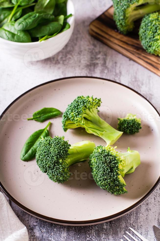 hojas frescas de brócoli y espinacas en un plato sobre la mesa. comida sana, comida verde. vista vertical foto