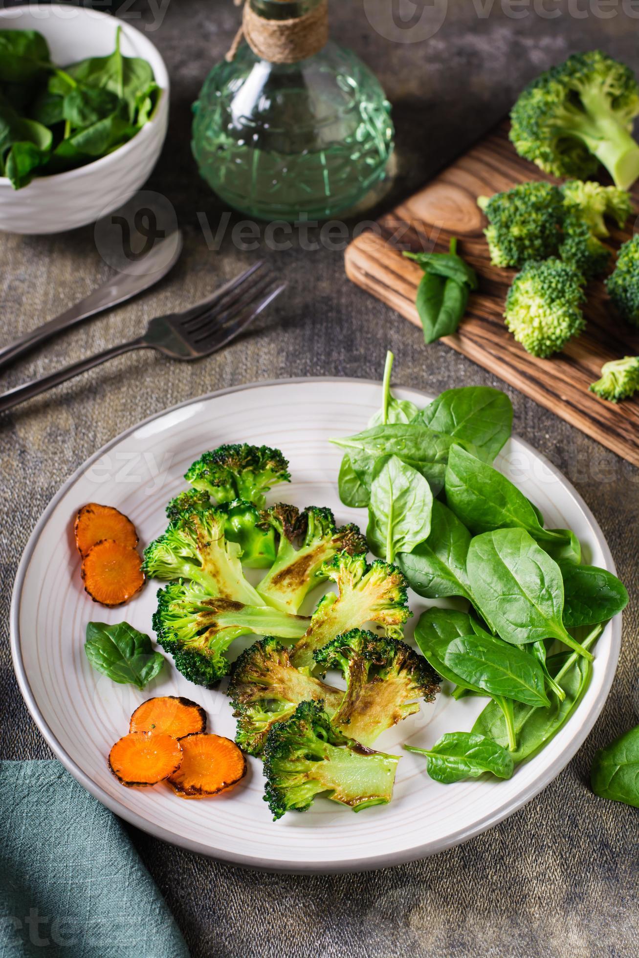 Grilled broccoli and carrots and fresh spinach leaves on a plate