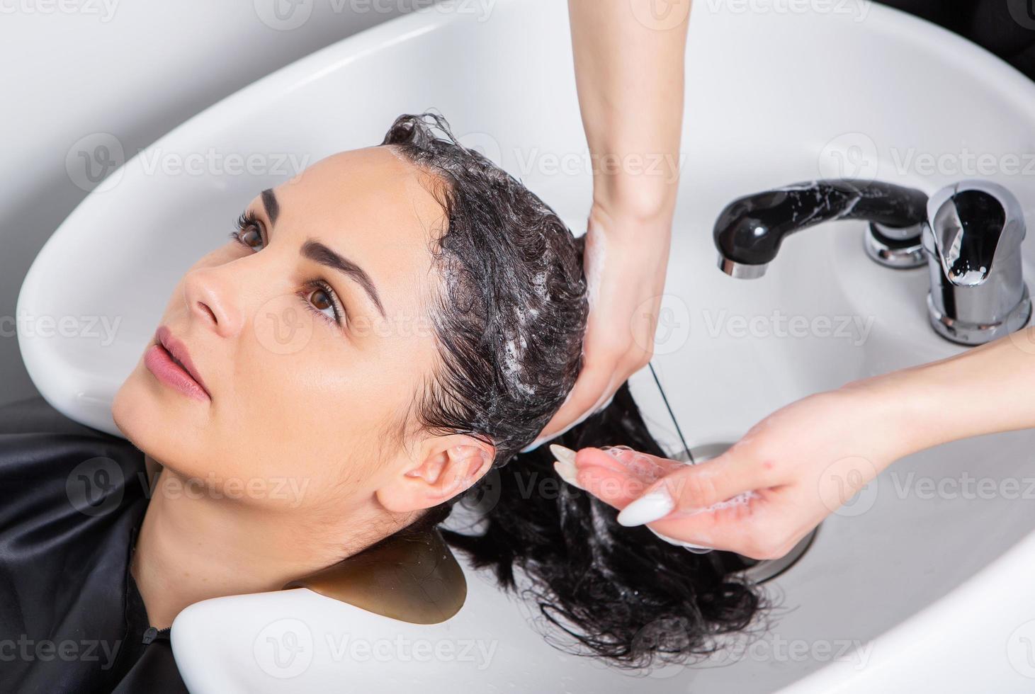 professional hairdresser washing hair of young woman in beauty salon photo