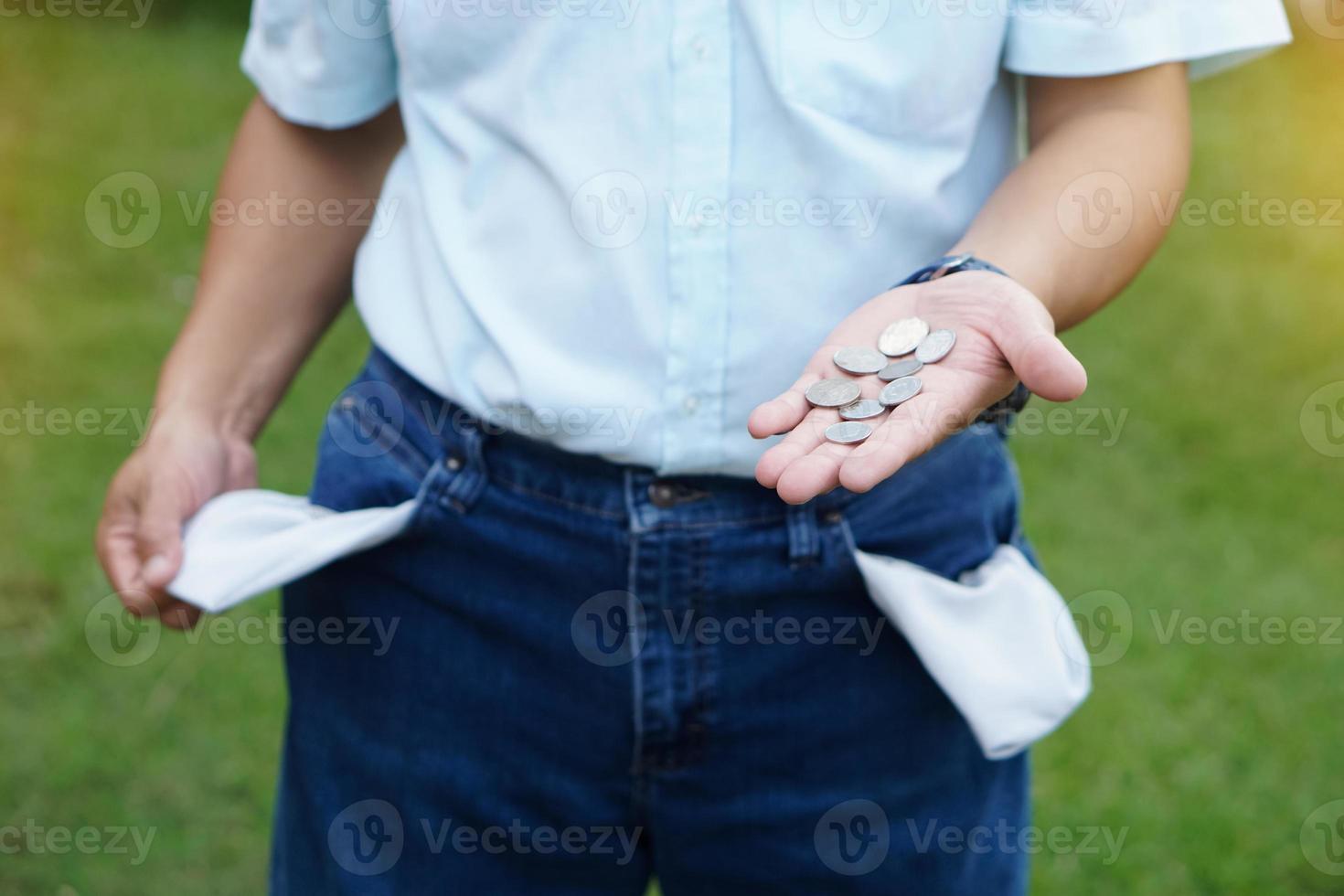 el hombre de primer plano usa jeans, sacando bolsillos para mostrar el bolsillo vacío. haga gestos con las manos para mostrar algunas monedas de dinero. concepto, crisis económica. problemas financieros. se rompió a fin de mes. dinero perdido. foto