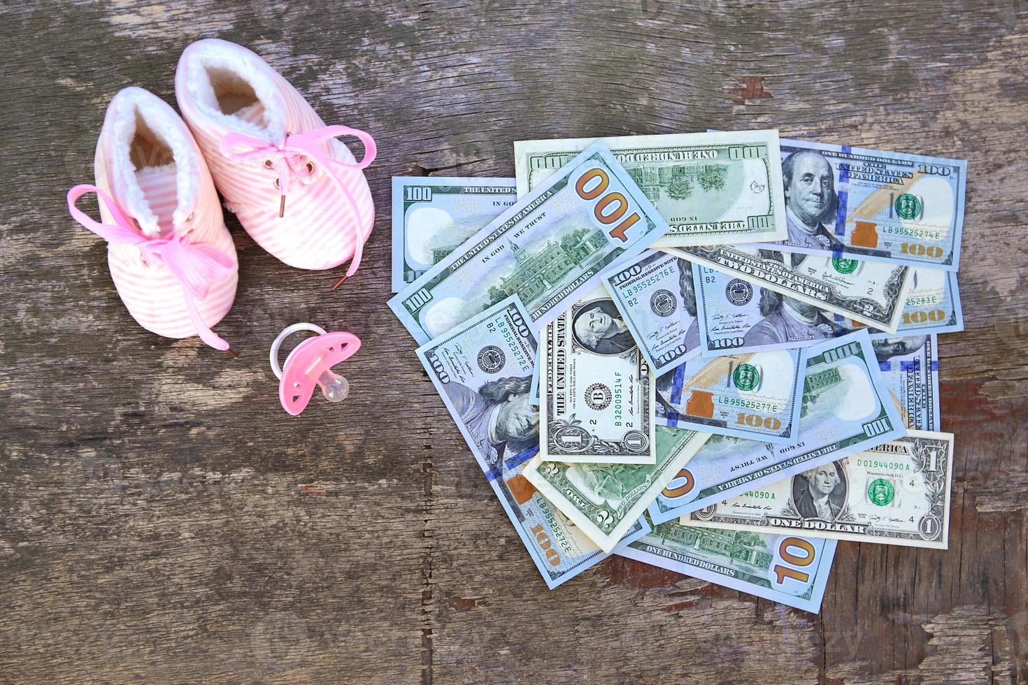 Pink pacifiers and children's shoes on the background of money. photo