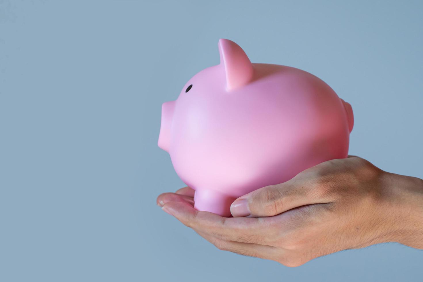 close-up hand holding a pink piggy bank isolated on blue background. money-savings concept. photo
