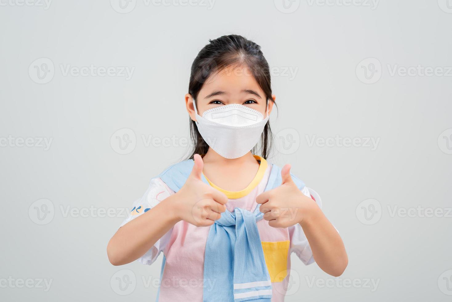 Asian little child girl wearing respirator mask to protect coronavirus outbreak and pointing hand to blank background, New virus Covid-19 photo