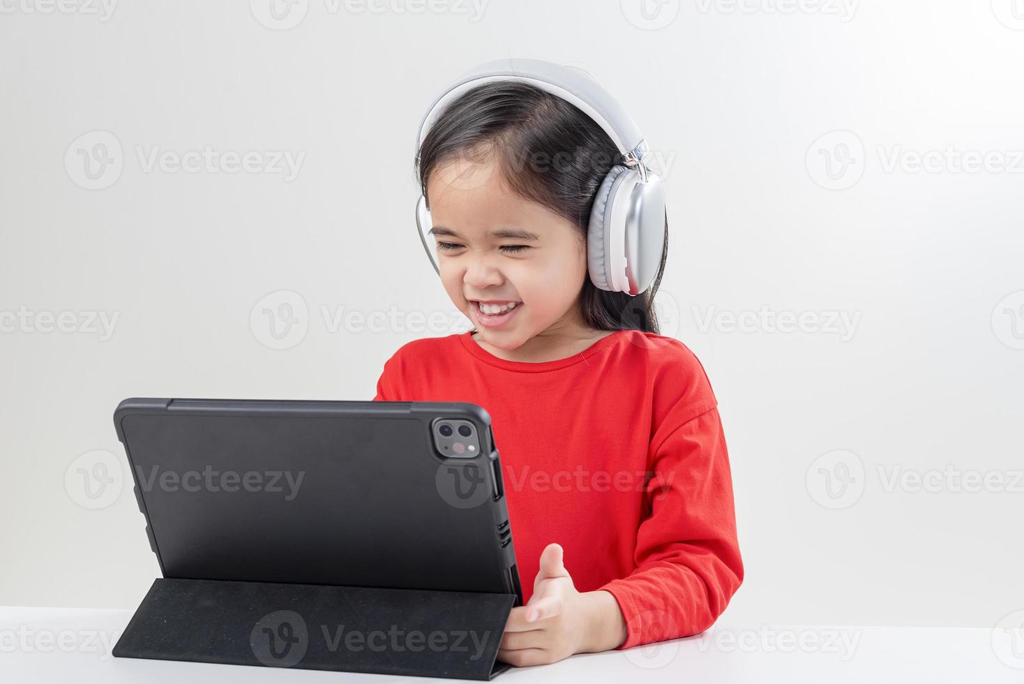 la niña asia linda se pone los auriculares tiene una videollamada clase distante con el maestro usando una computadora portátil, estudia en línea en la computadora, concepto de educación en el hogar foto