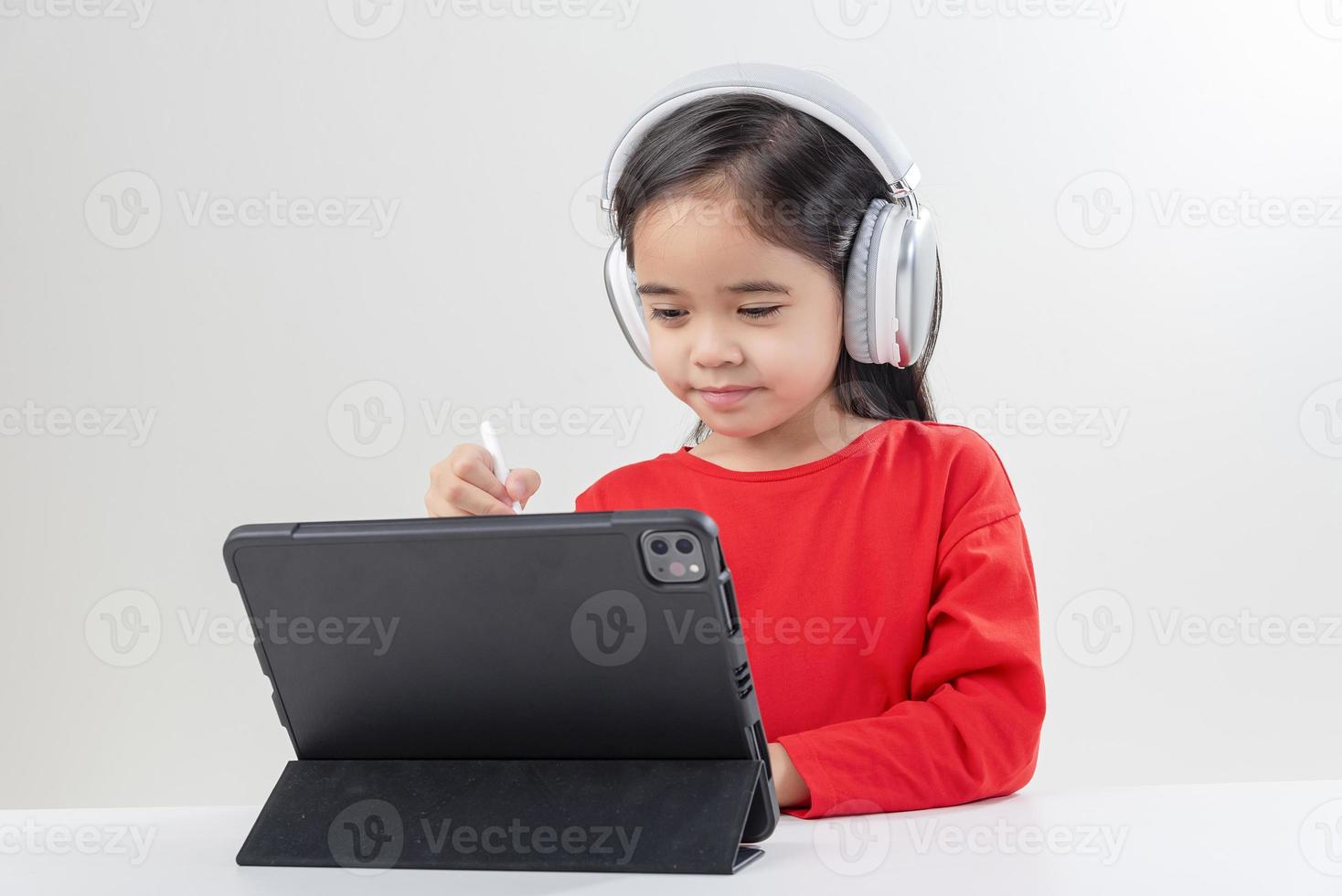 la niña asia linda se pone los auriculares tiene una videollamada clase distante con el maestro usando una computadora portátil, estudia en línea en la computadora, concepto de educación en el hogar foto