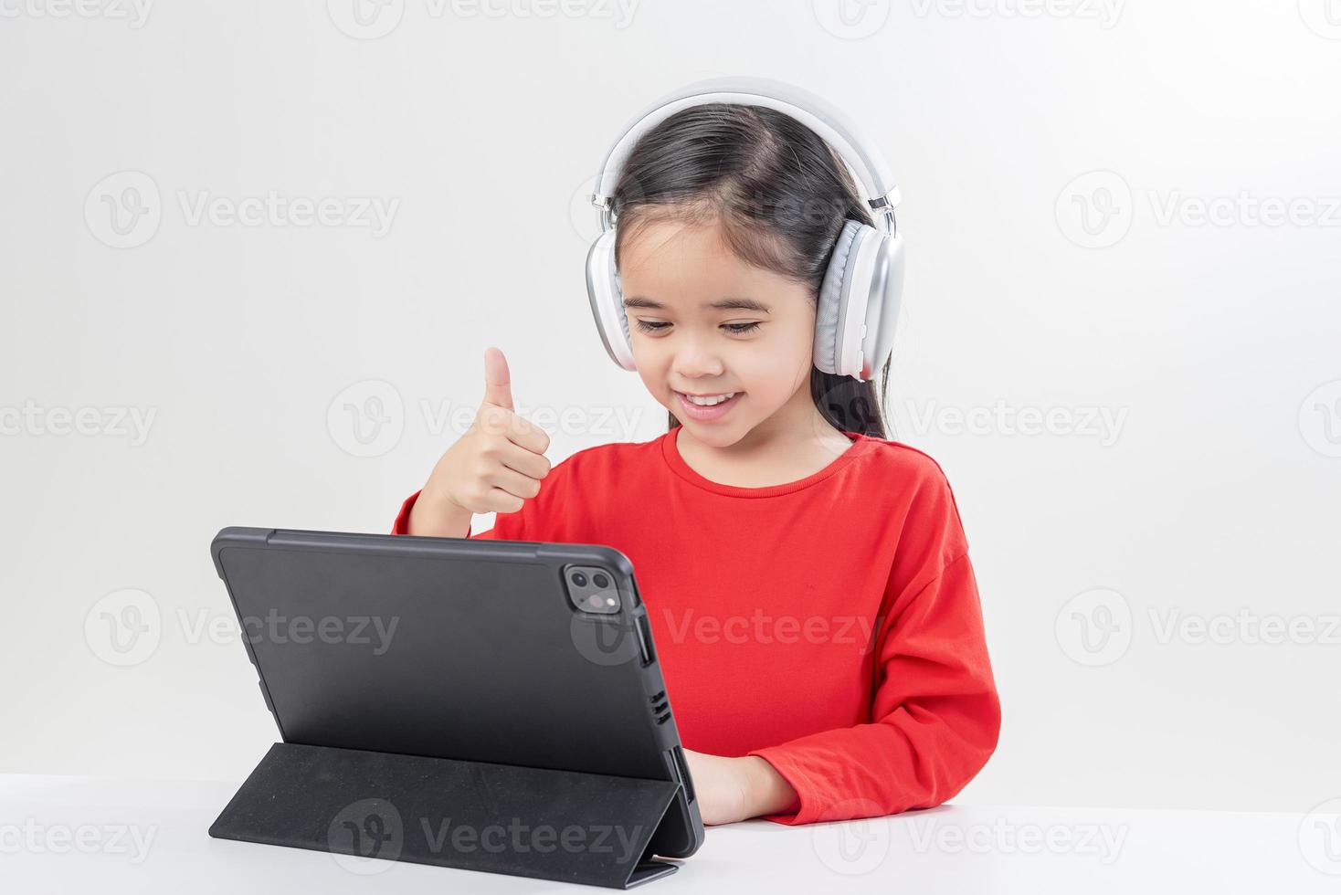 la niña asia linda se pone los auriculares tiene una videollamada clase distante con el maestro usando una computadora portátil, estudia en línea en la computadora, concepto de educación en el hogar foto