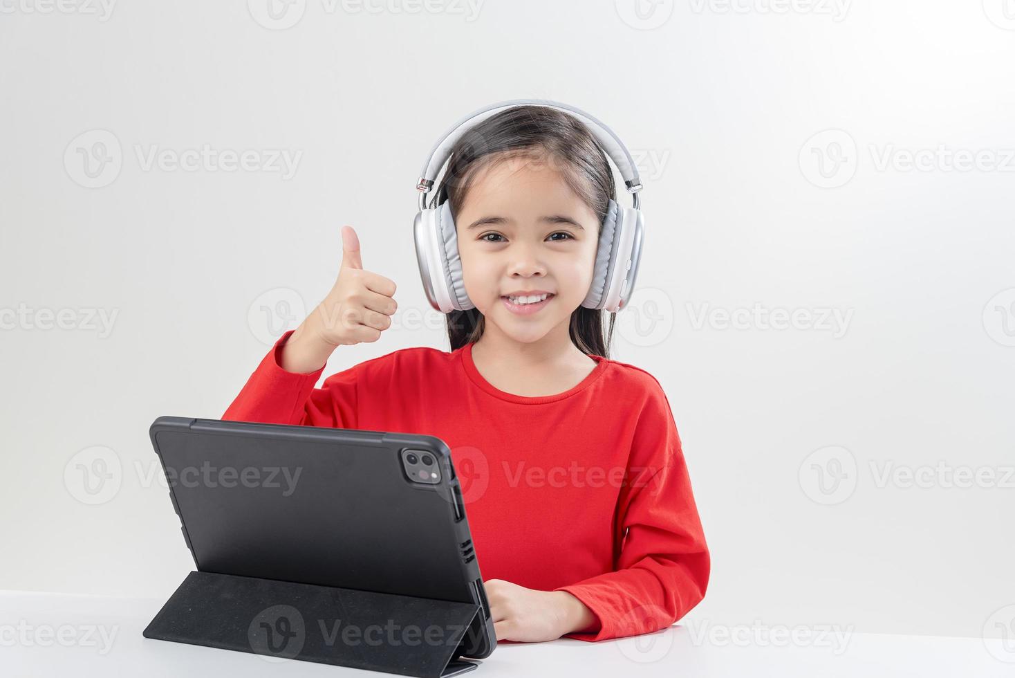 la niña asia linda se pone los auriculares tiene una videollamada clase distante con el maestro usando una computadora portátil, estudia en línea en la computadora, concepto de educación en el hogar foto