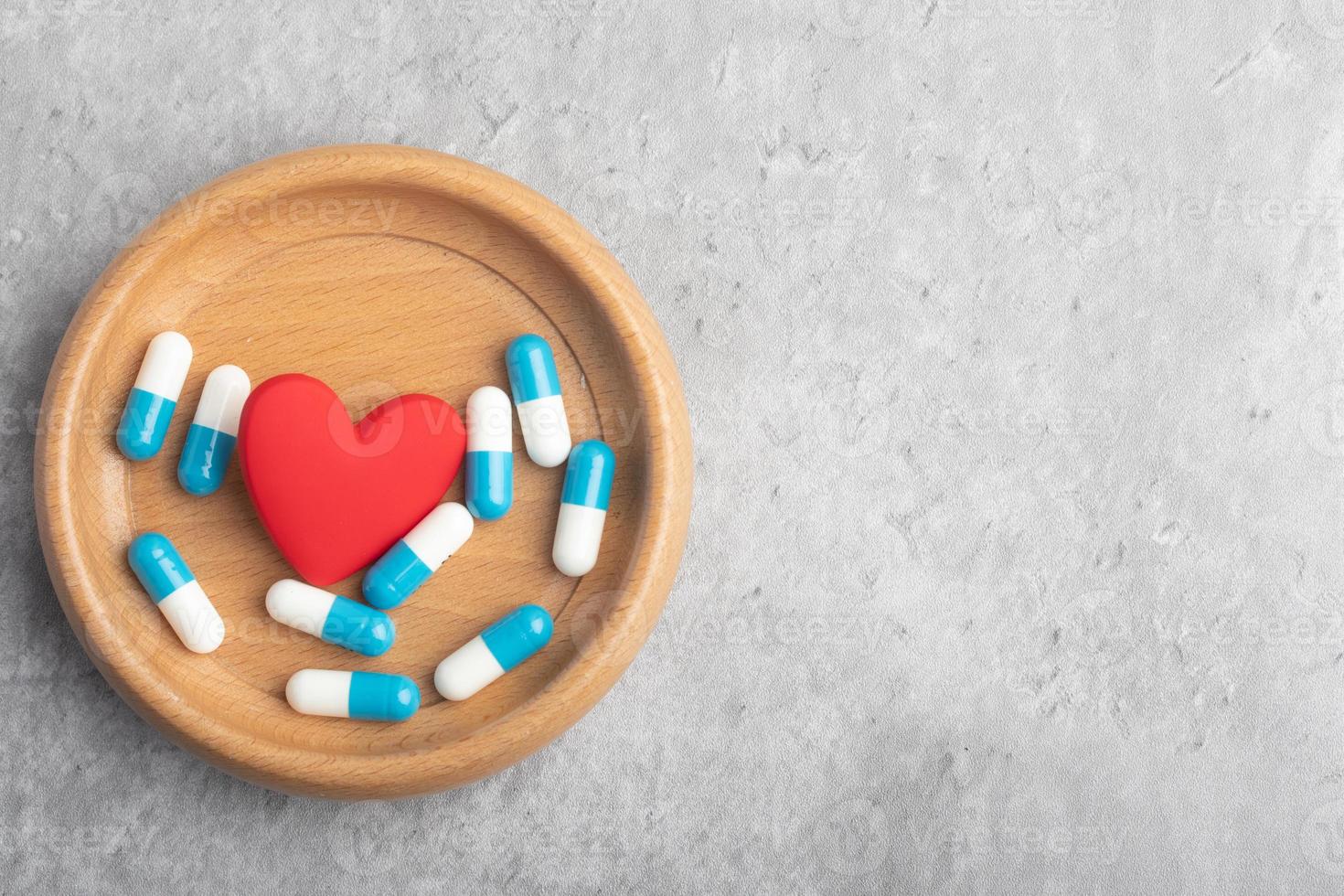 Medicine capsule and heart in wooden cup on gray background. Copy space. Medical treatment concept. photo