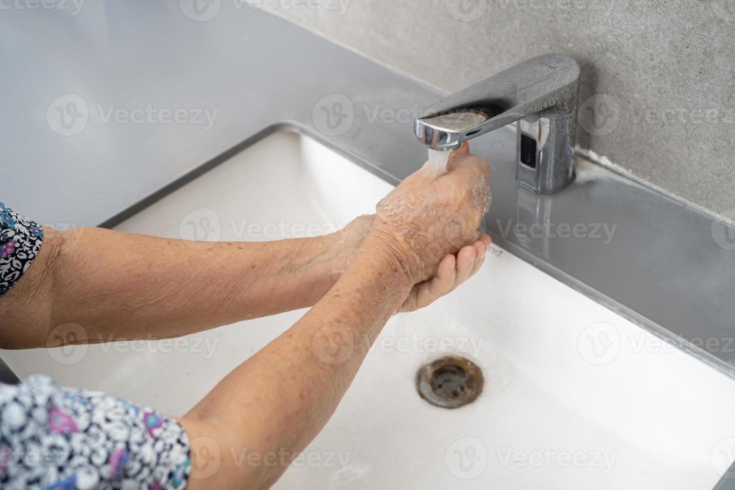 Asian senior or elderly old lady woman patient washing hand by soap and clean water for protect safety infection and kill Novel Coronavirus Covid-19 virus, bacteria and germs. photo