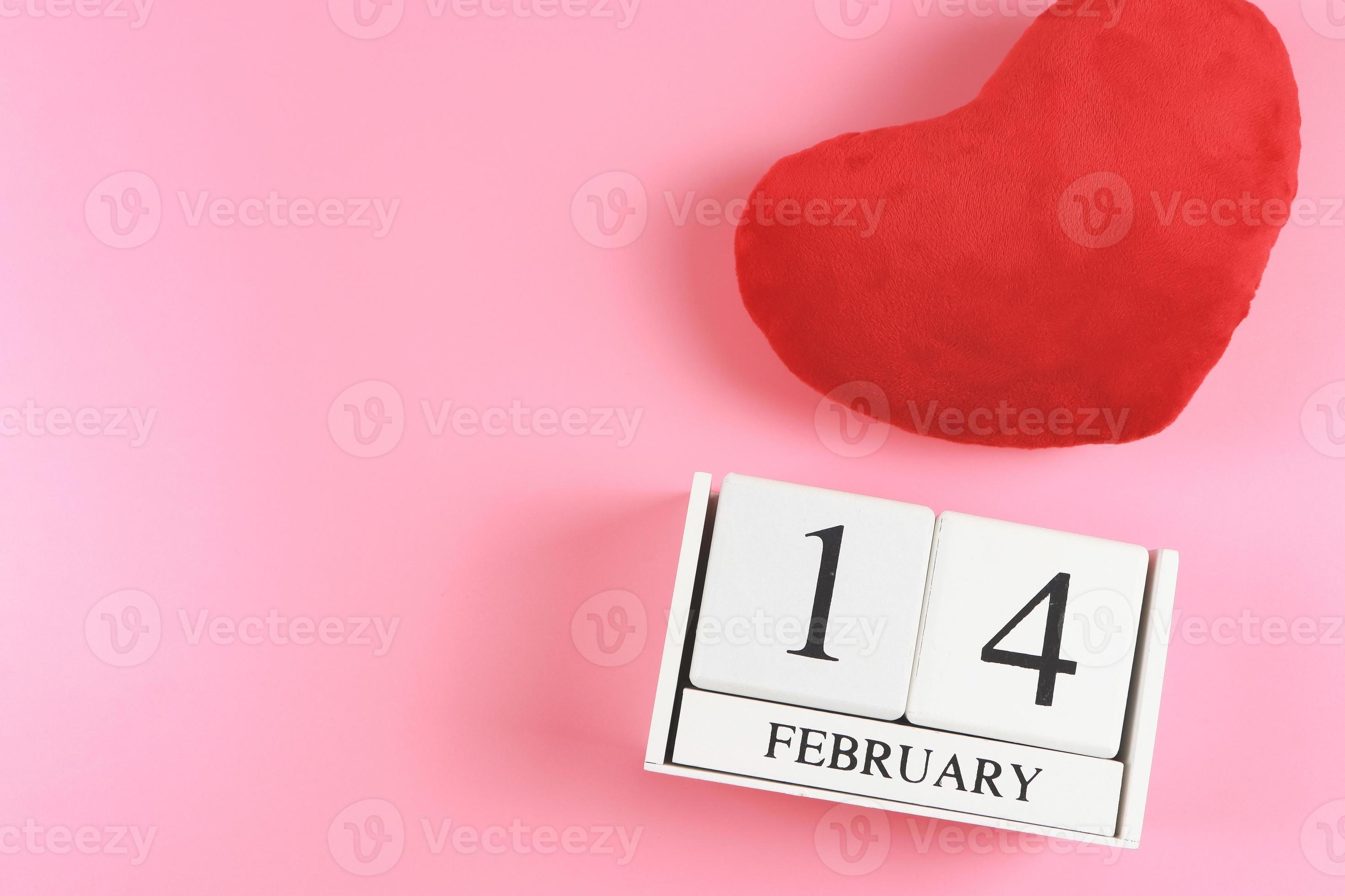 flat lay of wooden calendar February 14 with red heart shape pillow on